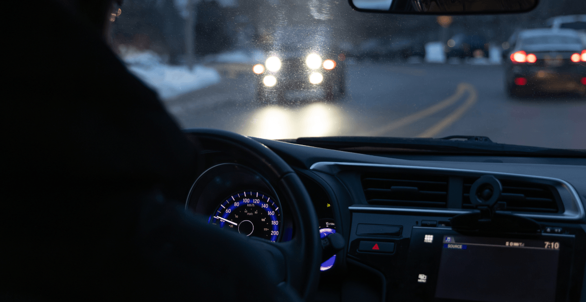 A car with bright headlights approaches another car on a two-lane road.