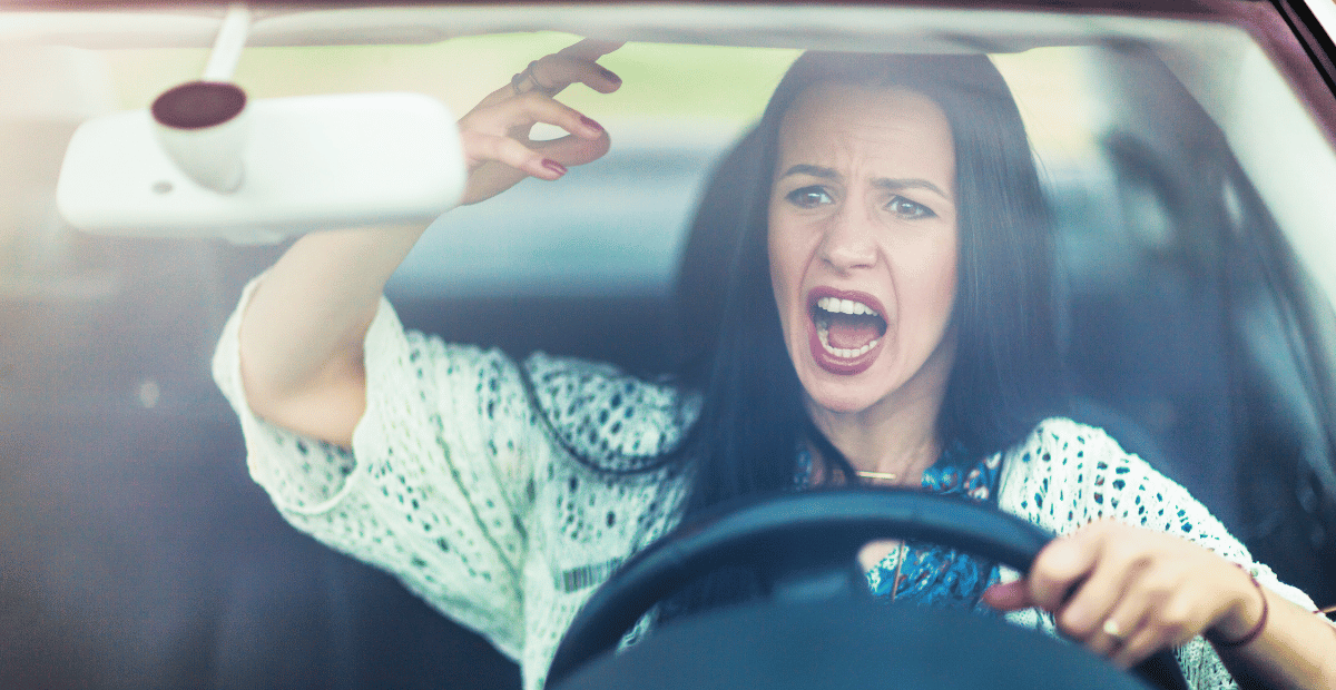 A woman at the steering wheel yells and gestures with anger.