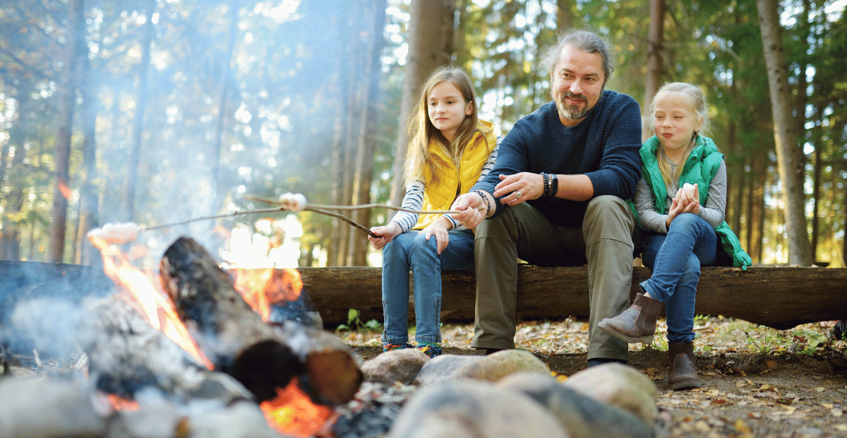 A father and his daughters roast marshmallows by the fire