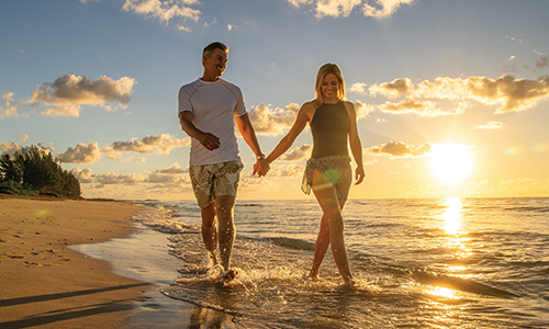 a couple walks on the beach at sunset