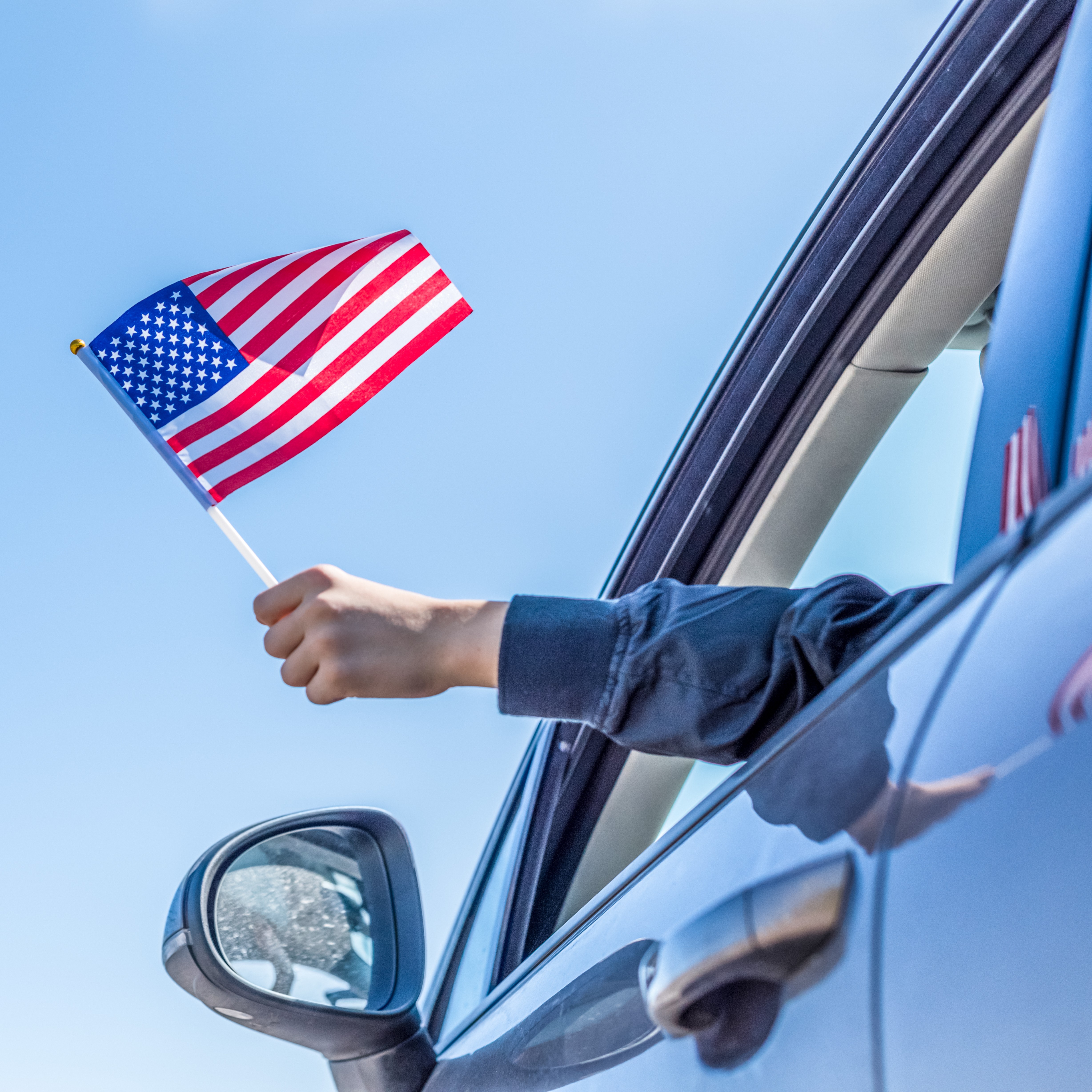 driver of car holds small American flag on a stick out window